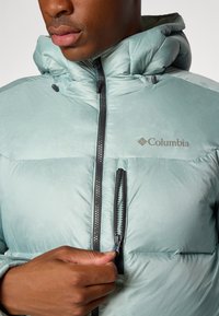 Light blue Columbia puffer jacket with a zippered front, hood, and side pocket. Features quilted texture and black zipper accents.