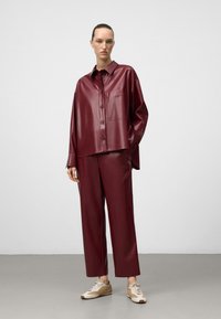 Burgunderfarbenes Kunstlederhemd und passende Hose mit lockerer Passform und Kragen. Sneakers mit beigen Akzenten ergänzen das Outfit.