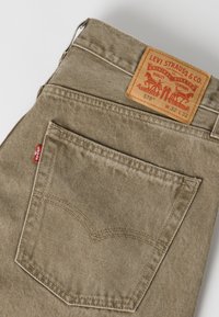 Μπεζ τζιν Levi's από denim διπλωμένα ώστε να φαίνεται η πίσω τσέπη, η κόκκινη ετικέτα Levi's και το δερμάτινο λογότυπο με μέγεθος W32 L32.