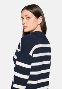 Polo en maille à rayures bleu marine et blanches, doté d'un col et d'une coupe décontractée, avec une texture lisse et des couleurs contrastantes en motifs horizontaux.