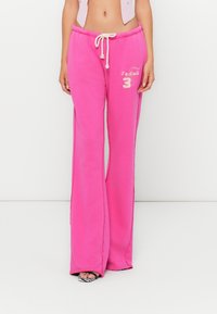 Pink flared sweatpants in cotton blend, featuring an elastic waistband with drawstring, graphic embellishment, and side slits.