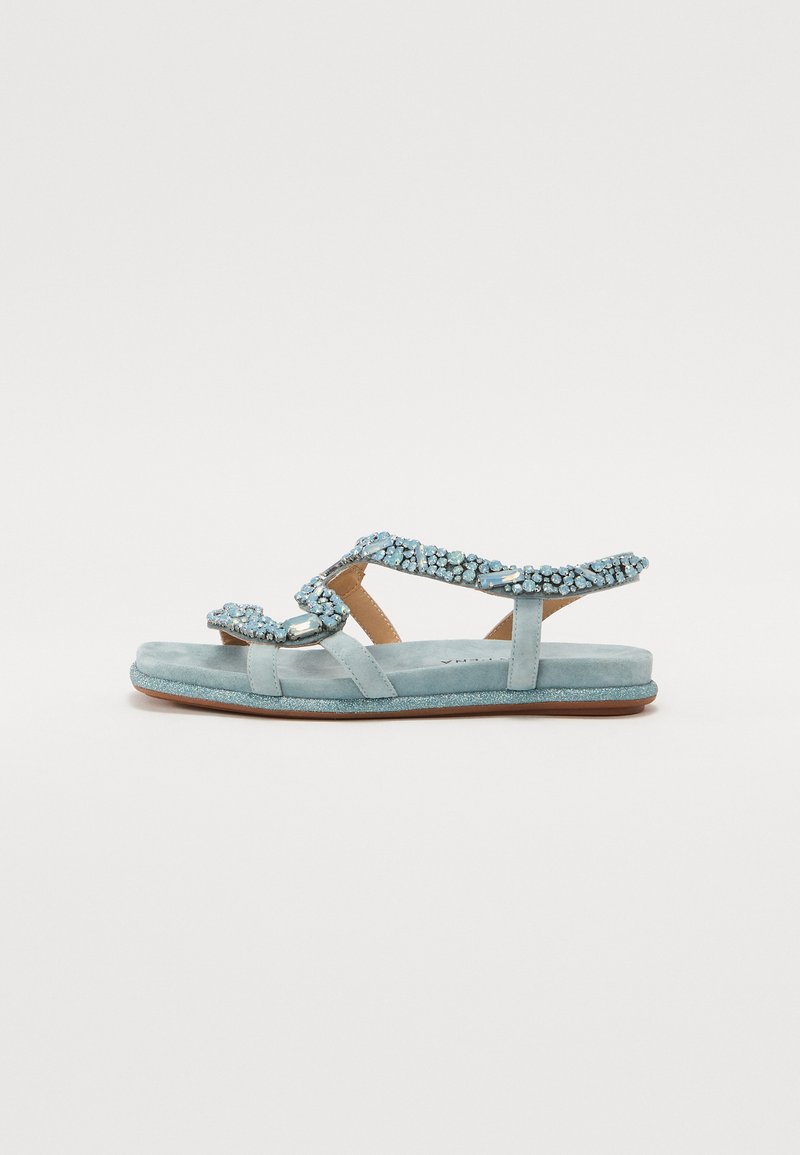 Sandales en suede bleu avec des lanières en bijoux, semelle plate et accents décoratifs. La texture est douce et la couleur est un ton aqua clair.