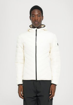 White padded jacket with a zigzag quilt pattern, black zip closure, and hood. Features a logo detail on the front and a smooth texture.