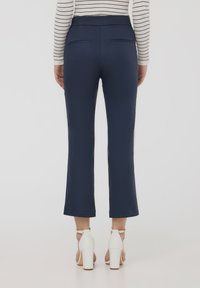 Pantaloni svasati blu navy con una trama liscia, caratterizzati da una vita alta e due tasche posteriori. Abbinati a sandali con tacco bianchi.