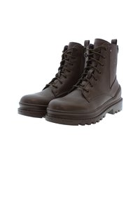 Botas de combate de piel marrón con cordones en la parte delantera, cremallera lateral y suelas de goma texturizadas. Presentan un detalle del logo y un diseño robusto.