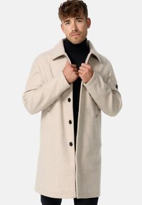 Beige uldblandingsfrakke med ombukket krave, fem forreste knapper og sidelommer. Glat tekstur og let oversized pasform.