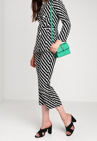 Pruhovaný černobílý outfit s peplum topem a zkrácenými kalhotami, doplněný zelenou kabelkou a černými sandály na blokovém podpatku.