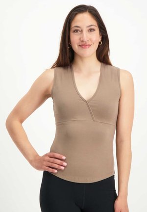 Körperbetontes ärmelloses Top aus weichem braunem Stoff mit tiefem V-Ausschnitt und einem strukturierten Mieder, kombiniert mit schwarzen Leggings.