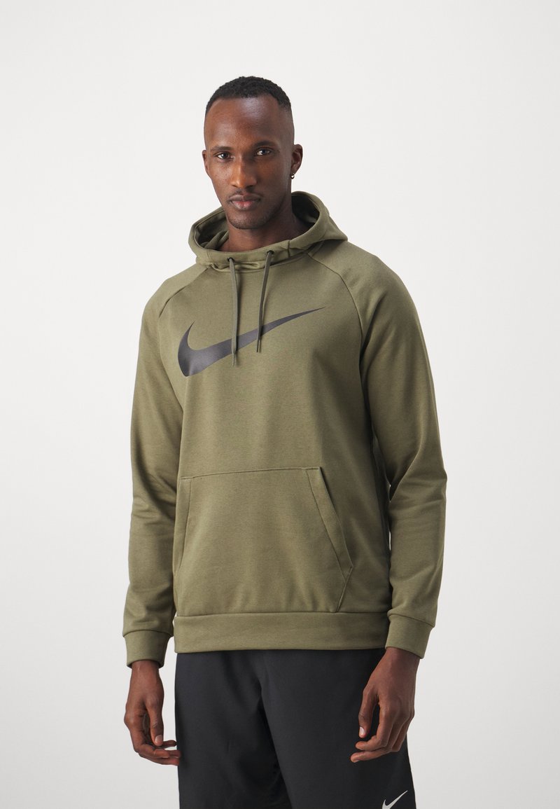Sudadera de Nike color verde oliva con un gran logo de swoosh negro, bolsillo tipo canguro, capucha con cordón y puños de canalé, combinada con pantalones negros.