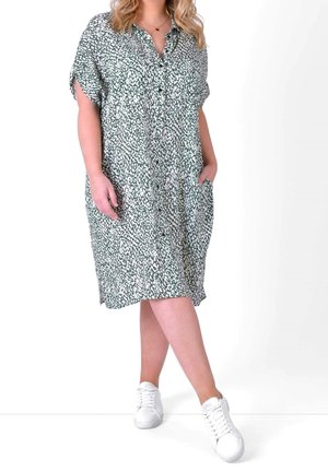 Zielono-biała sukienka koszulowa w wzory, z krótkimi rękawami, z przodu zapinana na guziki, z bocznymi kieszeniami i luźnym krojem, zestawiona z białymi trampkami.