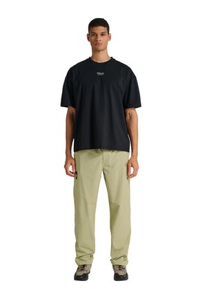 Zwart katoenen T-shirt met "HALO"-logo, gecombineerd met lichtgroene cargobroek met ritssluitingen en een losse pasvorm. Schoeisel is donkergroen met accenten.