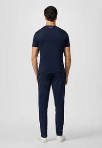 Mörkblå bomulls t-shirt med korta ärmar och rund halsringning, ihop med matchande joggers. Noterbar logotypdetalj på nacken.