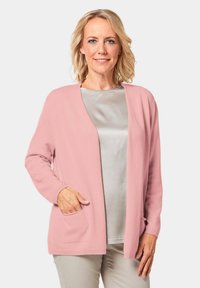 Helles rosa Cardigan mit lockerer Passform, offener Vorderseite und langen Ärmeln. Verfügt über Seitentaschen und gerippte Bündchen, über einem hellgrauen Oberteil getragen.