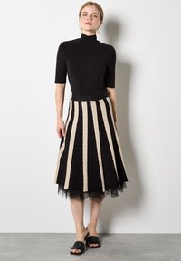 Top negro con cuello alto; falda acampanada con rayas verticales en negro y beige y una capa inferior de tul; zapatos negros de punta abierta.