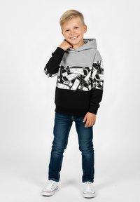 Szara i czarna bluza z kapturem z nadrukiem graficznym, z kieszenią kangurką i ściągaczami na rękawach, zestawiona z ciemnymi dżinsami i białymi trampkami.