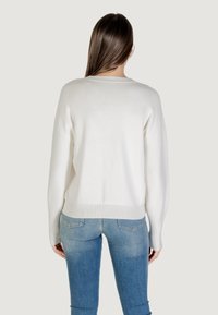 Witte gebreide trui met een relaxte pasvorm, geribde onderkant en mouwen, gedragen over lichtblauwe jeans, van achteren getoond.