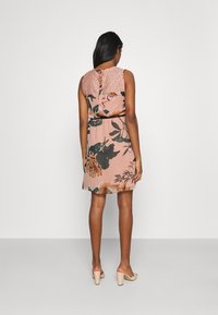Robe à imprimé floral en rose pâle avec un dos en dentelle texturée, taille cintrée et ourlet au niveau du genou. Accentuée par une fermeture à glissière cachée au dos.