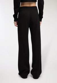 Czarne szerokie spodnie dresowe z elastycznym pasem, wykonane z miękkiego materiału, o gładkiej teksturze, bez widocznych wzorów ani ozdób.