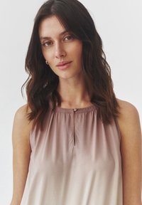 Haut sans manches avec un design ombré dégradé allant du rose clair au beige, présentant un col froncé et un petit détail en forme de œillet avec un bouton.