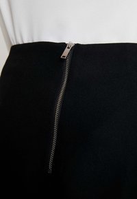 Gonna nera con una cerniera argentata sul lato e un tessuto strutturato e liscio. La parte superiore ha un design e una texture bianca e pulita.