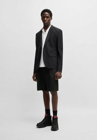 Black tailored blazer over a white button-up shirt and black shorts, paired with black high-top sneakers featuring red accents.