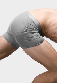 Pantaloni sportivi grigi con una vestibilità aderente, tessuto liscio, una vita ampia e dettagli delle cuciture discreti, mostrati da una prospettiva laterale durante il movimento.