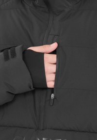 Svart pufferjacka med en dragkedjeförsedd bröstficka. Har en åtsittande manschett med tumhål och textil med struktur som ger isolering och komfort.