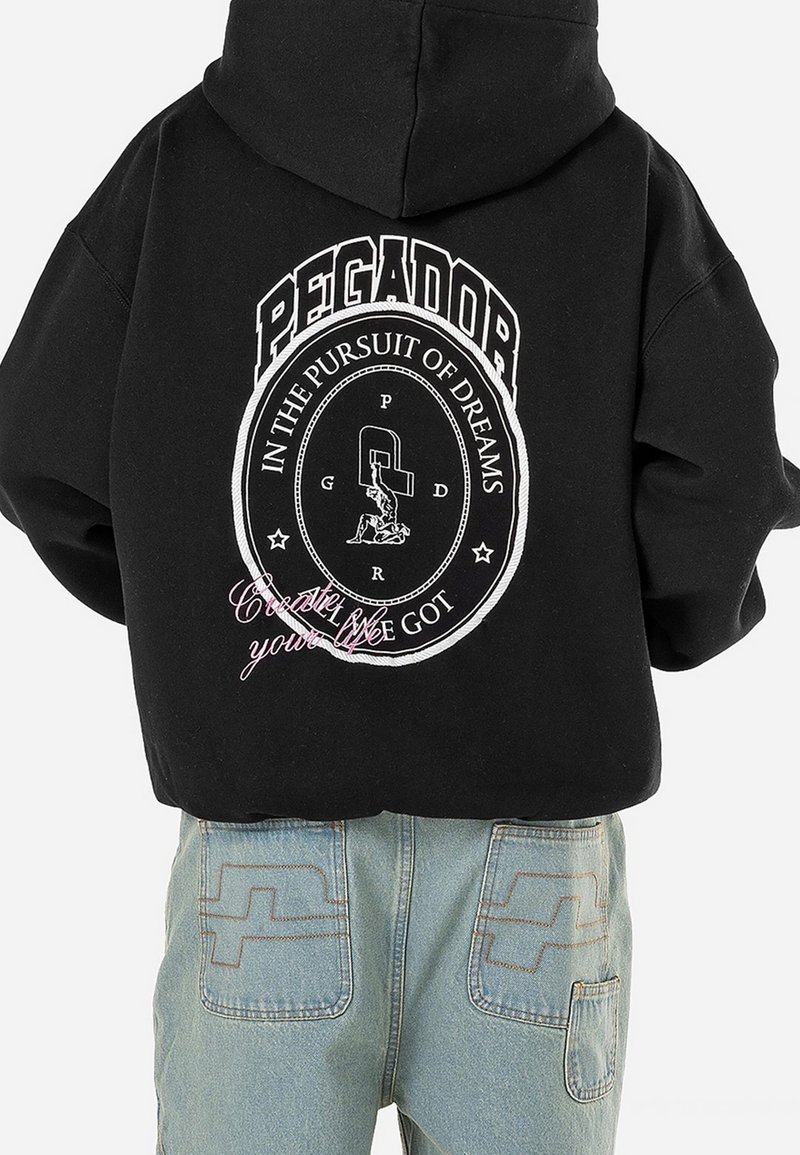Sweat à capuche noir avec un graphisme circulaire blanc et le texte "PEGADOR", "IN THE PURSUIT OF DREAMS" ainsi qu'une écriture rose "Create your life" au dos.