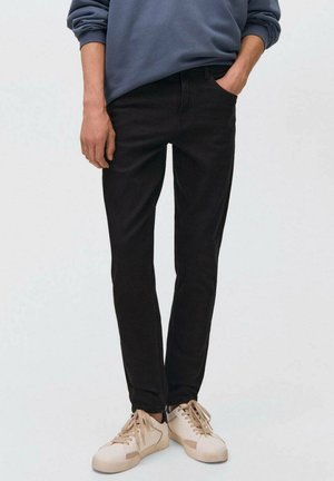 Jean oscuro de mezclilla con corte slim, dos bolsillos laterales y un ligero brillo, combinados con zapatillas beige y una sudadera azul.