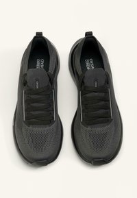 Czarne buty sportowe z siateczkową cholewką, teksturowanym wzorem, okrągłym noskiem, elastycznymi sznurowadłami oraz pętelką na pięcie ułatwiającą zakładanie.