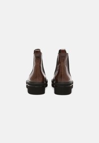 Par de botas de cuero marrón hasta el tobillo con suelas gruesas negras, vistas desde atrás sobre un fondo blanco.