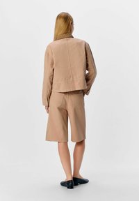 Beige denimjacka och shorts set med en strukturerad passform. Har bröstfickor och matchande shorts med bakfickor. Platta skor.
