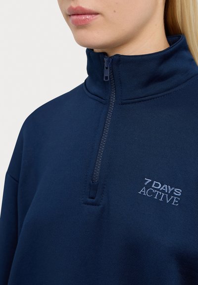 Navy blue quarter-zip sweatshirt made of soft fabric, featuring a high collar and an embroidered "7 DAYS ACTIVE" logo on the chest.