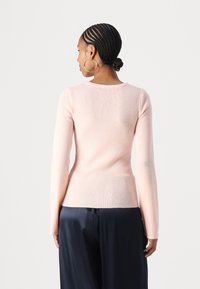 Maglione lungo a maniche lunghe di un rosa chiaro a coste, con una silhouette aderente, scollatura rotonda e pantaloni scuri a contrasto. Texture morbida con una leggera elasticità.