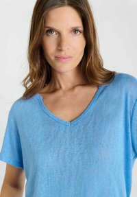 Lichtblauw katoenen T-shirt met een V-hals en korte mouwen, uitgevoerd in een textuur met een licht doorschijnende stof. Eenvoudig en casual ontwerp.