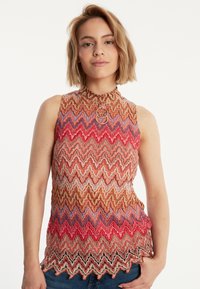 Ärmelloses Oberteil mit wellenförmigem Muster in Rot-, Blau- und Brauntönen; verfügt über einen hohen Kragen und ein kreisförmiges Hardware-Detail am Ausschnitt.