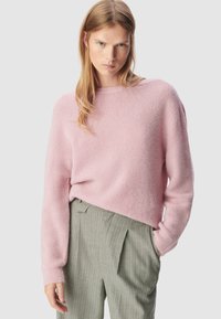 Jasnoróżowy puszysty sweter z okrągłym dekoltem i długimi rękawami, w połączeniu z zielonymi spodniami w paski o wysokim stanie z zakładkami.