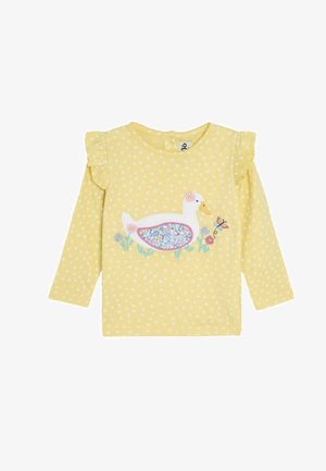 Gul langærmet skjorte med hvidt blomstermønster, flæser ved skuldrene og et ande-tryk omgivet af blomster og en sommerfugl.