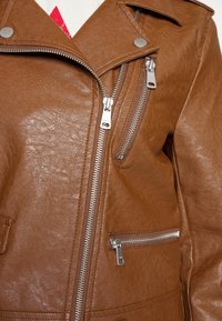 Veste de moto en similicuir marron avec fermetures éclair argentées, col à revers et plusieurs poches zippées. Fini texturé et lisse.