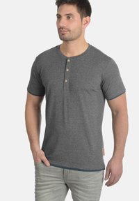 Graues Kurzarm-T-Shirt mit rundem Halsausschnitt, ausgestattet mit Holzknöpfen und blauen Akzenten an den Ärmeln, aus weichem Baumwollstoff gefertigt.
