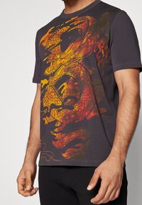 Camiseta de algodón negra con un vibrante diseño gráfico de dragón en rojo y naranja. Mangas cortas y cuello redondo estándar. Textura suave.