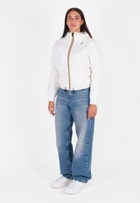 Witte zip-up jas met een capuchon, voorzien van een meerkleurige rits. Gecombineerd met lichtblauwe, wijde jeans en witte sneakers.