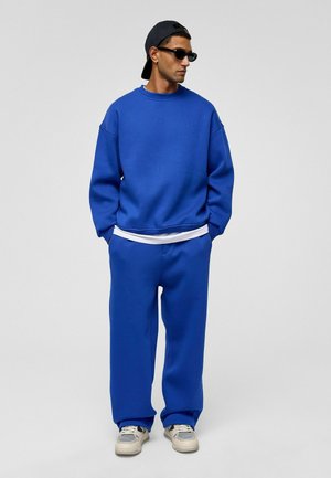 Blauwe sweatshirt en bijpassende broek, gemaakt van zachte katoenmixstof. Losse pasvorm met ribgebreide manchetten en details, gedragen met een witte T-shirt eronder.