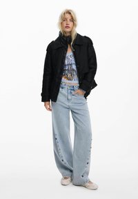 Must mustrinna musteri kottja tumedatest puffer jakist, prinditud sinine tank top all, laiad helesinised teksad külgmiste nupuvajutustega ja beežid slip-on kingad.