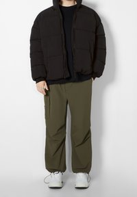 Svart puffjacka med dragkedjestängning och texturerade paneler, kombinerad med olivgröna cargobyxor och vita sneakers.