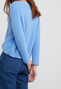 Light blue knitted sweater with a wide neckline and long sleeves, featuring a textured pattern, paired with blue jeans.