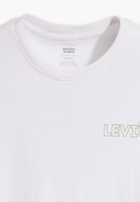 Biała bawełniana koszulka z okrągłym dekoltem i logo 'Levi's' w jasnym beżu. Posiada luźny krój i gładką fakturę.