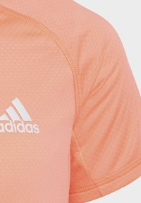 Camiseta atlética de color naranja claro con tela texturizada, que presenta el logo blanco de Adidas, mangas cortas y costuras en contraste a lo largo de las costuras.