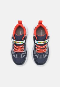 Sapatilhas navy com detalhes em vermelho, uma fita de velcro com "SUPER MARIO" e sola branca. Parte superior em tecido texturizado com detalhes em design riscado.