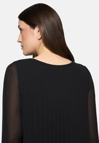 Czarna sukienka o miękkiej, plisowanej fakturze z przezroczystymi długimi rękawami. Dekolt jest okrągły, podkreślający smukłą sylwetkę.